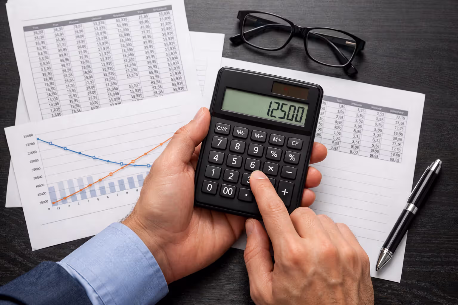 Close-up of hands using calculator next to printed financial amortization schedules and documents on office desk